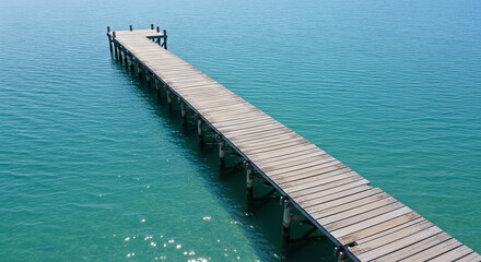 aerial view of empty pier extending into calm ocean, clear blue water all around
