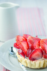 Strawberry Tart with Whole Strawberries. A delicious, glazed strawberry tart on a plate with two whole, fresh strawberries placed in the foreground.