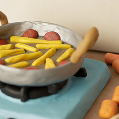 Colorful clay cooking scene with frying pan, vegetables, and stove on neutral background