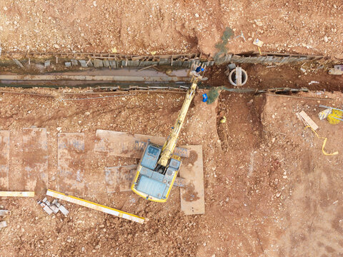 Worker on Excavator Bucket, Construction Site Installing Pipes