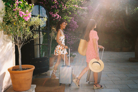 Two young women pulling suitcases on vacation arrive at hotel