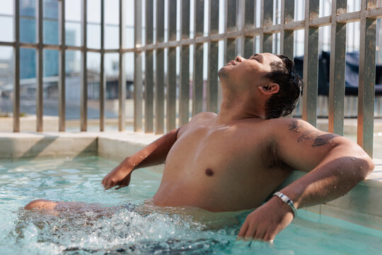Man relaxes in rooftop pool, eyes close and face tilted toward the sun