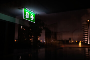Green exit sign glows in dark, reflecting city lights.