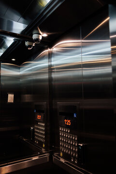 Shiny elevator interior with security cameras and floor buttons.