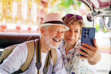 Closeup American senior couple tourist take a photo selfie in a Tuktuk Thailand taxi on blurred sun bright background. Senior tourist concept