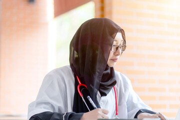 Closeup a beautiful Asian female doctor in hijab traditional clothes and medical shirt doing a...