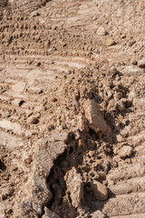 close-up of a rugged, brown dirt terrain showing detailed textures with prominent clumps and tire tracks, highlighting a natural outdoor landscape during daylight, rural, outskirts, patterns