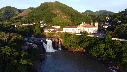 Fototapeta premium Waterfall cascading into a river valley with lush green mountains and historical buildings
