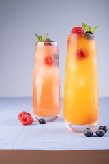 refreshing fruit-infused summer drinks in tall glasses with ice cubes, garnished with fresh raspberries, blueberries, and mint leaves on a soft blue surface, decorative, tempting, gradient, colorful