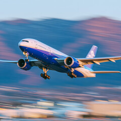 Obraz premium A blue and white airplane takes off against a backdrop of purple and orange sunset hues, with blurred mountains in the distance, showcasing motion and speed.