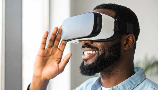 A smiling young African American man wears a modern virtual reality headset, interacting with an immersive digital world. He looks happy and engaged. - Powered by Adobe