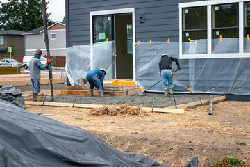 Construction workers in rubber boots and hard hats working cement pumper hose to pour fresh cement...