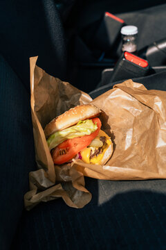 Closeup of cheeseburger on car seat with soda bottle nearby