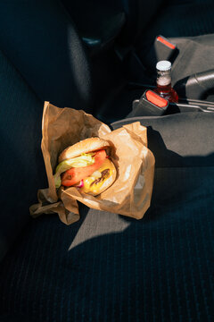 Cheeseburger in paper wrap on car seat with bottle in background