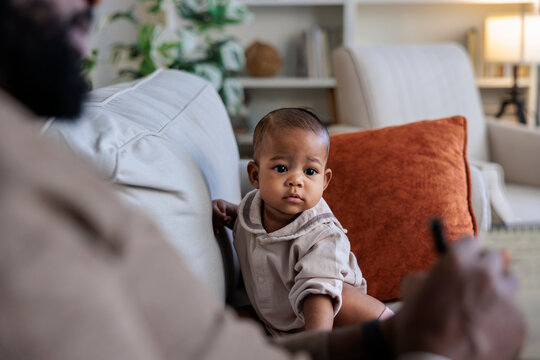 Baby on couch looks at dad writing notes.