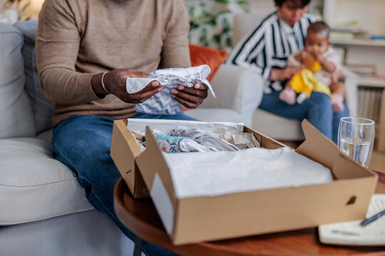 Father unpacks baby clothes while mother holds baby.