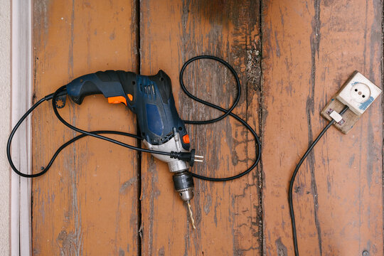Corded drill on wooden floor next to electrical outlet