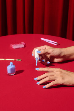 A close-up of hands applying blue nail polish to painted nails