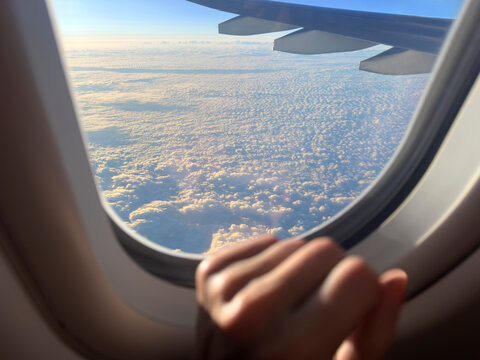 Hand on an airplane window and clouds in the sky