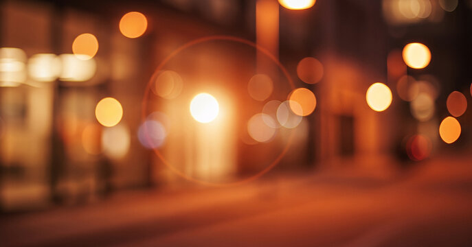 Blurred street scene at night illuminated by warm orange and yellow bokeh lights, adding a glowing charm to the bustling nighttime atmosphere.