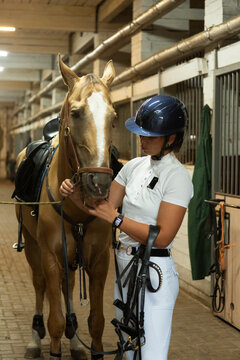 Female jockey preparing horse for equestrian competition in stable