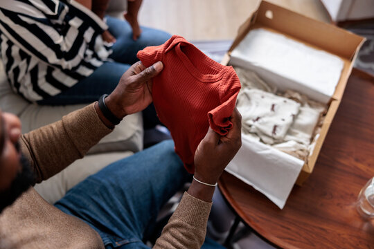 Parent unpacking baby clothes from a box.