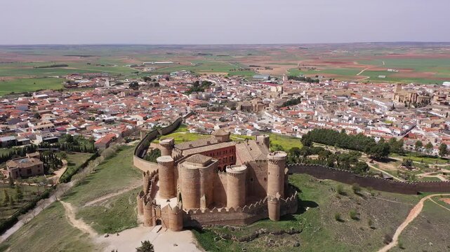 View from drone of Castillo de Belmonte, ancient walled fortified castle on background of townscape and extensive agricultural fields on sunny spring day, Spain