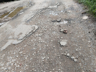 damage poor road and rain water. cracked old asphalt in need of repair. The road is full of holes and potholes.