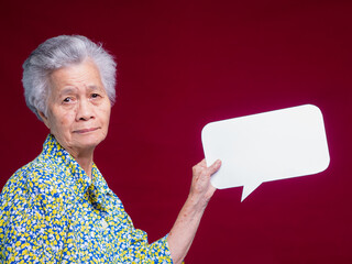 Elderly Asian woman holding blank speech bubble on red background for communication concept.