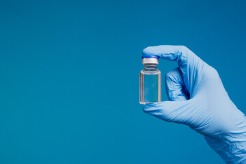 Hand in blue medical glove holding vaccine vial on blue background for healthcare and immunization...