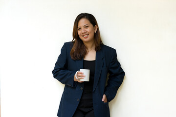  Professional woman standing while holding a white mug, dressed in a navy blue blazer, looking to...