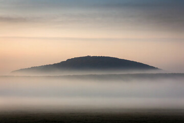 Fototapeta premium Tranquil landscape featuring a misty forest and a mountain during a serene sunrise or sunset