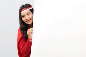 Indonesian woman with the concept of celebrating Indonesian independence peeking behind a blank...