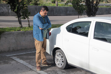 Adult Latino dark-skinned man suffers a car accident and has a flat tire and has to change it