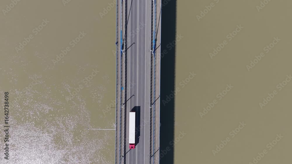 Poster aerial view of vehicles traveling across a bridge over a wide brownish river. the symmetrical compos