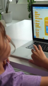 A child in a purple shirt engaged in STEM programming on a laptop, bright natural light, indoor setting, close-up, vertical video, ideal for mobile and social media platforms.