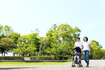 石畳の新緑のある公園をベビーカーを押し散歩する若い夫婦