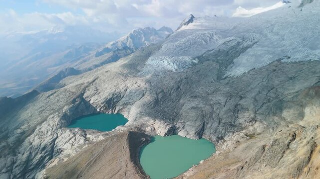 Aerial pan revealing the dramatic rocky terrain, glacial slopes, and twin turquoise lakes of Paso del Zorro high in Peru&rsquo;s Cordillera Blanca mountains.
