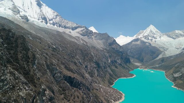 A stunning, high-altitude aerial shot slowly pans to reveal the vast, vibrant turquoise waters of Laguna Par&oacute;n and the spectacular snow-capped peaks of the Andes in Peru.