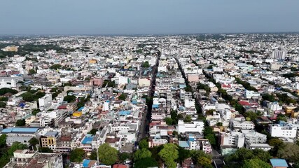 This aerial footage presents a wide, high-angle view of densely populated city. A long, straight road acts as a central axis, with countless low-rise buildings extending to the horizon on both sides.