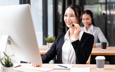 A smiling and friendly female customer service representative wearing a headset works at a computer...
