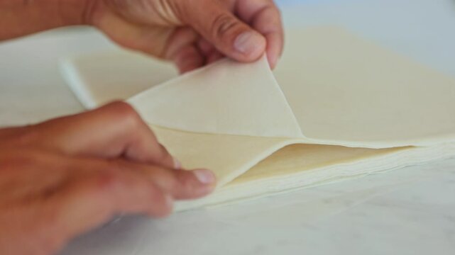 Chef folding rice paper wrappers on puff pastry to prepare spring rolls