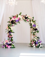 A floral archway, abundant with pink, purple, and white blooms, stands against a white backdrop