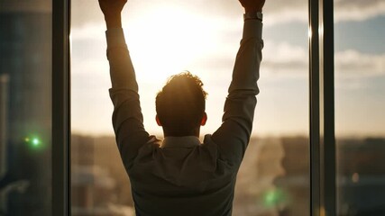 Happy office worker throws their arms up in celebration, silhouetted against a large window with bright sunlight streaming