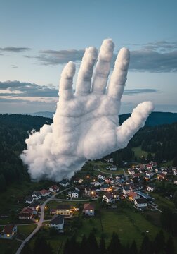 Cloud hand floats above a quiet village at dusk, representing the surreal connection between nature and the human imagination.