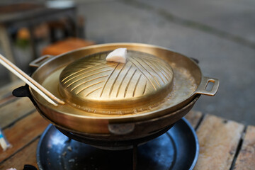 BBQ pan made of brass, Pork fat loaf on the top of the pan. Its name is called moo ka ta, a popular food among Thai people on holidays
