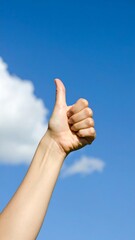 Hand giving thumbs up against a blue sky