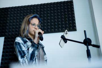 Lifestyle portrait of a teenage girl singing into a microphone in a professional recording studio....