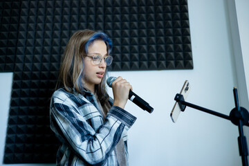 Lifestyle portrait of a teenage girl singing into a microphone in a professional recording studio....