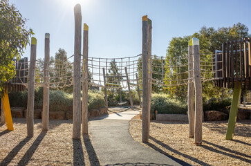 Modern outdoor playground with a rope bridge and tall timber posts, featuring an integrated...